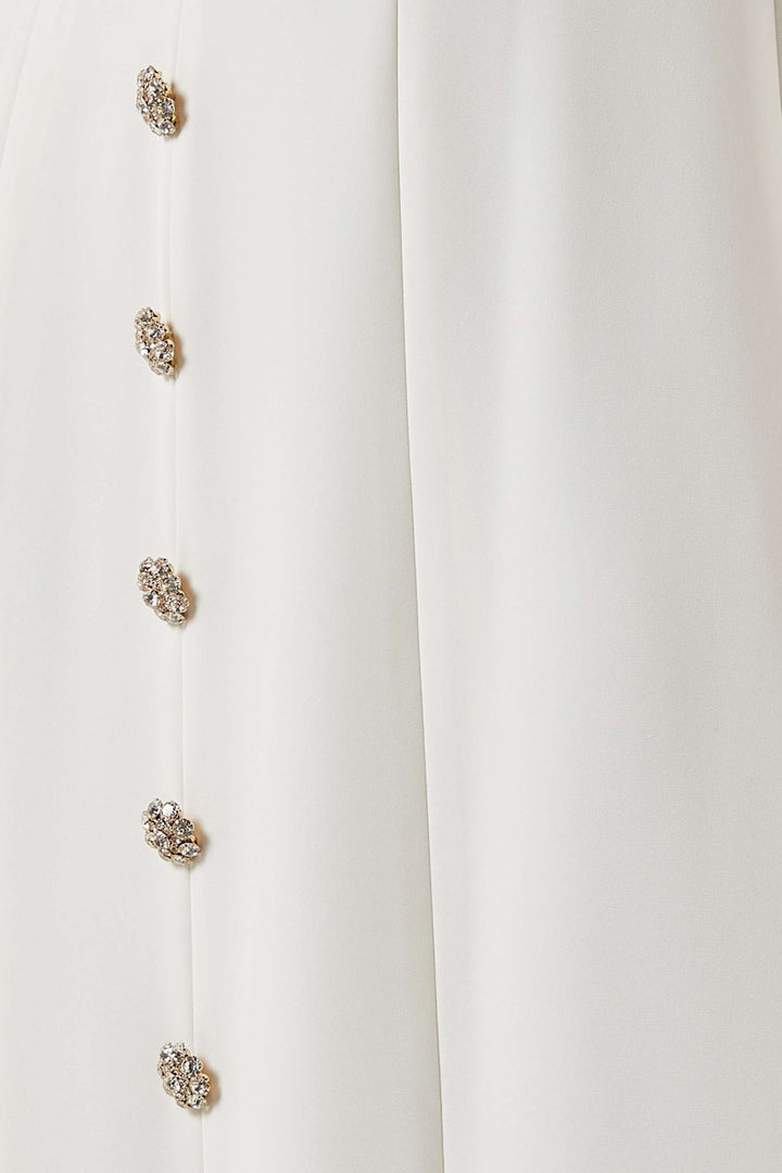فستان بفتحة رقبة منسدلة وأزرار مرصعة بالجواهر – عاجي